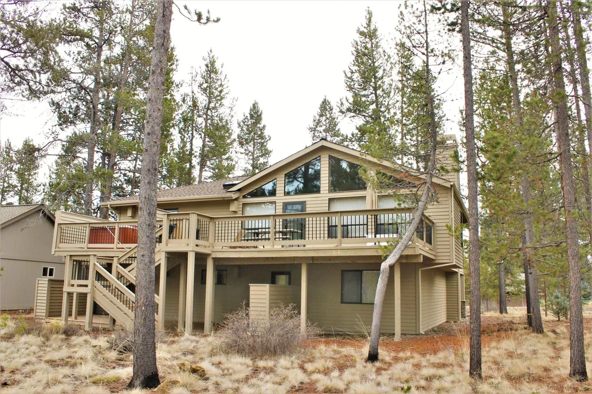 This image captures the exterior of the house with its expansive deck area surrounded by towering trees. The deck is set up for gatherings, with ample space for outdoor dining and relaxing, and provides a clear view of the serene natural landscape with no neighboring homes in sight.