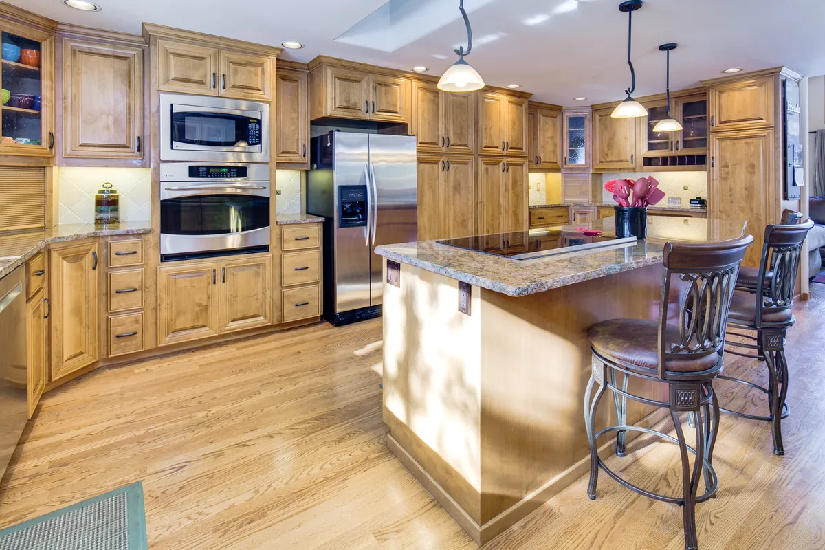 A well-appointed kitchen with a central granite island, wood cabinetry, and stainless steel appliances. The space is designed for cooking, entertaining, and culinary gatherings, with ample room for several people to interact.