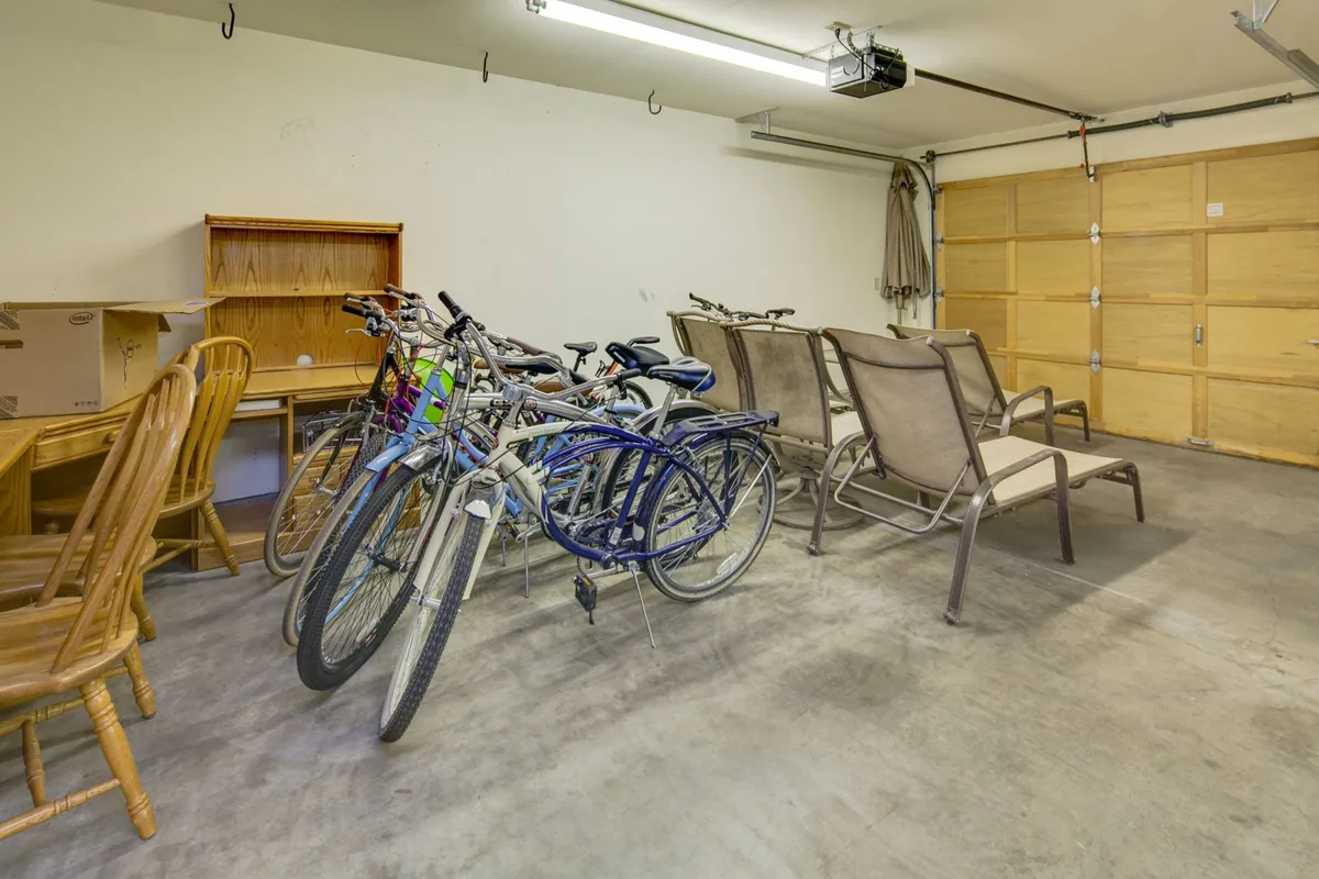 The image shows a clean, organized garage space with bicycles neatly stored, a couple of chairs, and storage shelving along the walls. The area is well-lit and welcoming, highlighting the available bikes for guest use and the practical nature of the space for storing outdoor gear.