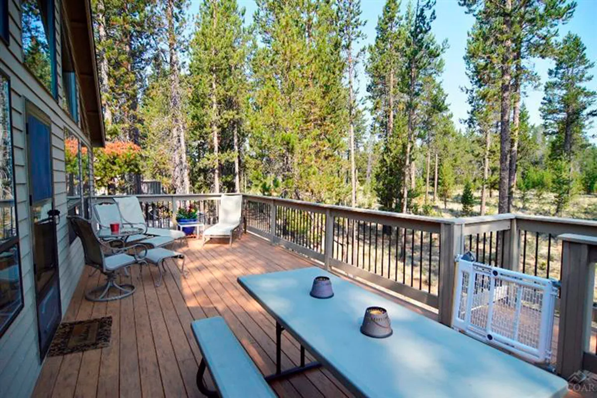 This exterior shot focuses on the wooden deck, equipped with deck chairs and an outdoor table, all framed by lush trees. The peaceful ambience is perfect for socializing, reading, or stargazing at night, reflecting the deck's role as a central hub for relaxation and al fresco dining.